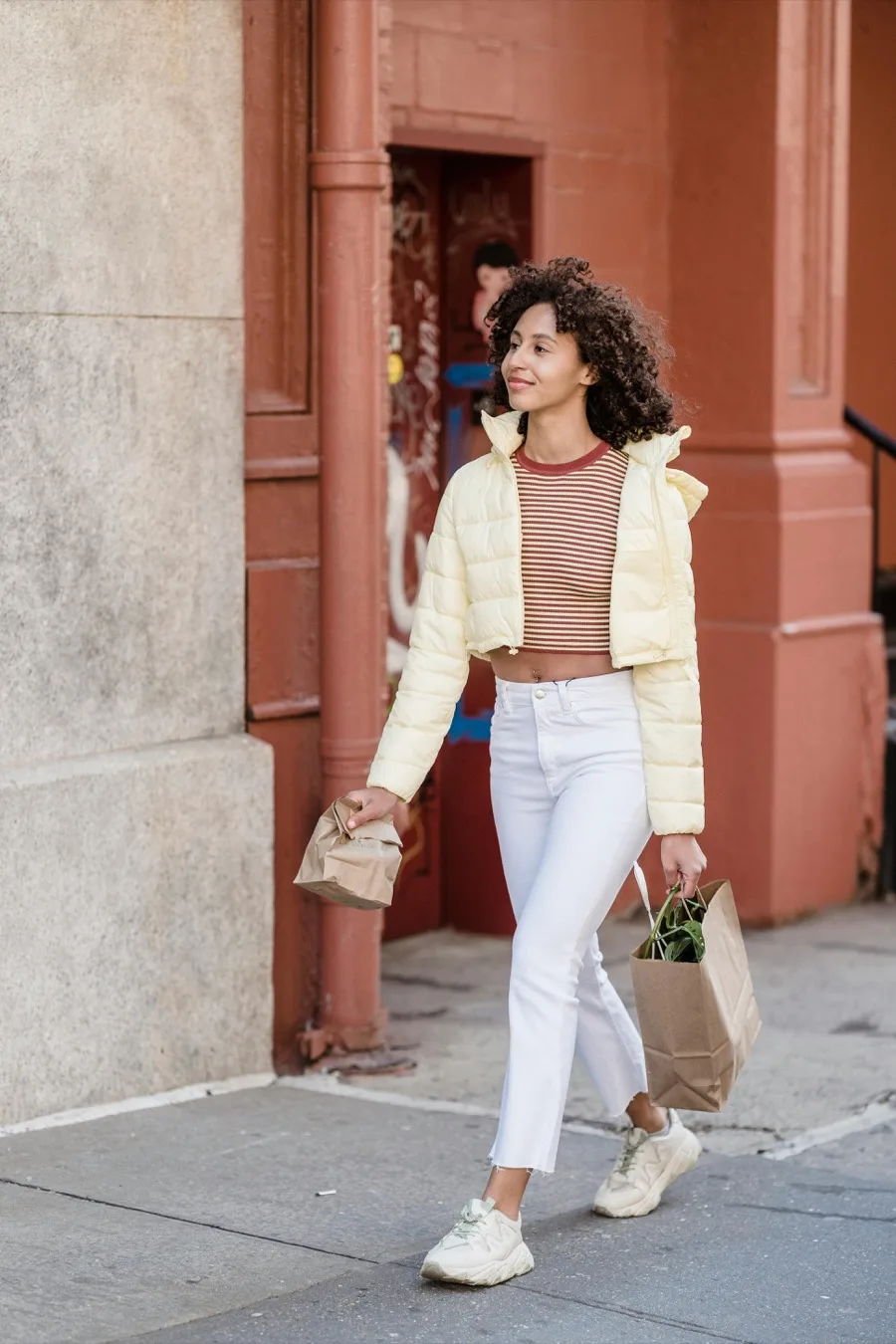 Yellow puffer jacket with striped crop top and white jeans